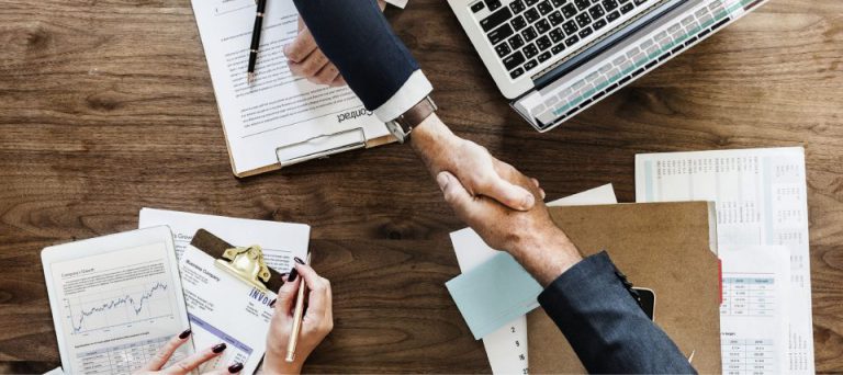 Overhead view of two people shaking hands across a desk of documents and a laptop