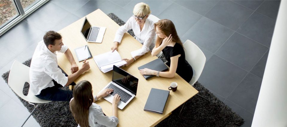 Overhead view of colleagues meeting around a white table with tablets and notebooks