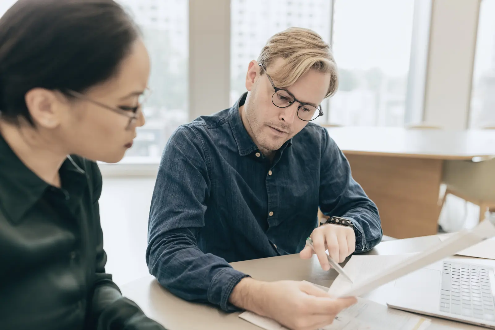 Two colleagues review a printed document together at a desk